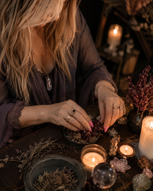 Belinda preparing herbs and candles for a Blockbuster Road Opener Spell at a private candlelit ritual altar with warm spiritual energy.